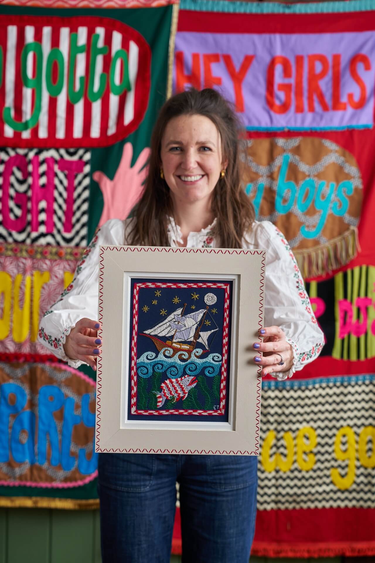 Eppie Thompson founder of The Fabled Thread inside her embroidery studio with ship and sea embroidery kit in frame